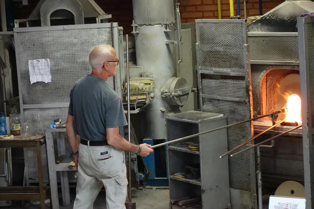 Vidriero frente a la boca encendida de un horno de taller, con la caña de soplar apoyada en el brazo
